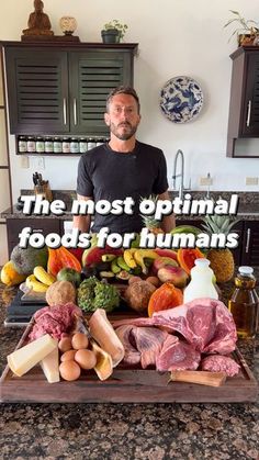 a man standing in front of a table filled with fruits and vegetables, next to a cutting board that says the most optimal foods for humans