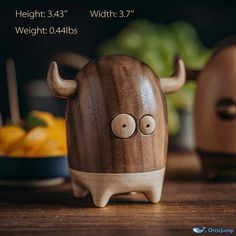 a wooden toy with horns and eyes sitting on a table next to some fruit in bowls