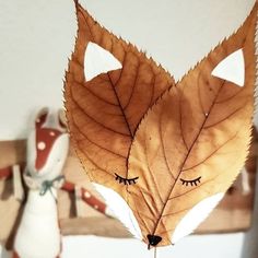 a close up of a leaf with eyes drawn on it's face and another stuffed animal in the background