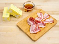 slices of bacon sit on a cutting board next to butter, butter cubes and honey