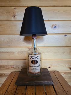 For sale we have an amazing table top lamp made with a upcycled Tito's Vodka bottle. This bottle is the 1.75 liter glass that is mounted on a 9" x 11" wood base plate hand stained mahogany color. This lamp features rubber anti slip feet and a 8' long high quality new power cord. Each lamp comes with a new  9 watt LED bulb. The lamp overall height with the lamp shade is 20". This lamp was just handmade and ready to light up your room. The new black lamp shade is included, you may request a white Alcohol Bottle Lamp, Bourbon Bottle Lamp, Jack Daniels Bottle Lamp, Man Cave Lighting, Liquor Bottle Lamp, Full Liquor Bottle Lamp, Steam Punk Lamp Using Liquor Bottle, Table Top Lamps, Black Lampshade