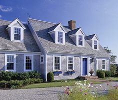 a large gray house with white windows and shingles on the roof, surrounded by greenery