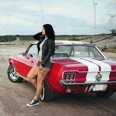 a woman sitting on the hood of a red and white car in front of wind mills