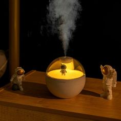 an aroma diffuser sitting on top of a wooden table next to two small figurines