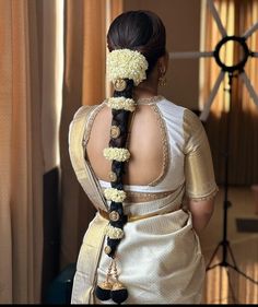 a woman wearing a white sari with flowers in her hair is looking out the window