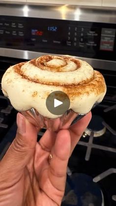 someone is holding up a cinnamon roll in front of an oven