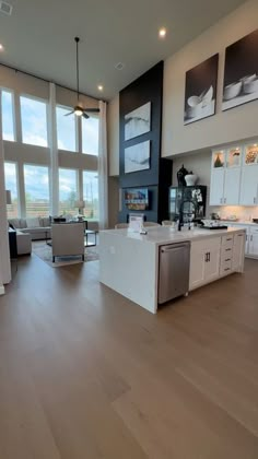 a large open living room and kitchen area with wood flooring, white cabinets and windows