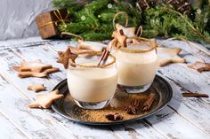 two glasses filled with drink sitting on top of a plate next to cookies and cinnamon sticks