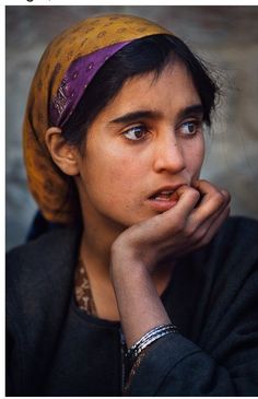 a woman wearing a head scarf and looking off to the side with her hand on her chin