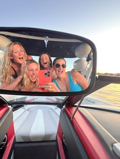 four women taking a selfie in the rear view mirror of a boat on water