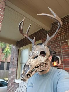 a man wearing a deer mask with antlers on it's head, standing in front of a house