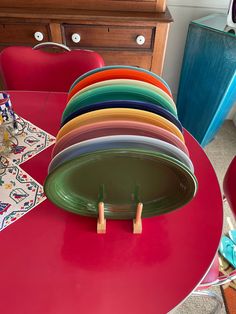 a stack of plates sitting on top of a red table next to a wooden dresser