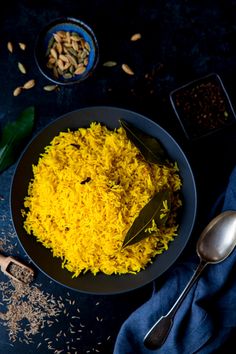 yellow rice in a black bowl with spoons and spices on the table next to it