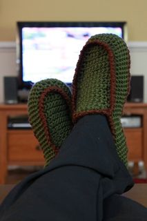 someone's feet wearing mittens in front of a television set with the tv on