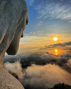 the sun is setting over some clouds in the sky behind a statue with its eyes open