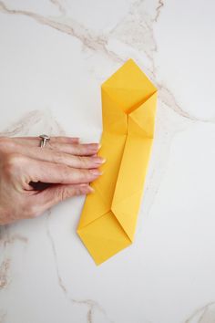 a woman's hand holding an origami tie on top of a table