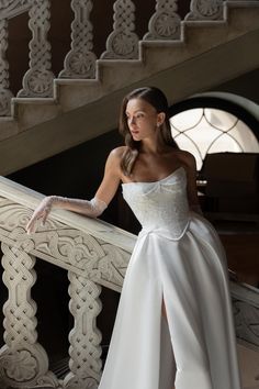 a woman in a white dress standing on a stair case with her hand on the railing