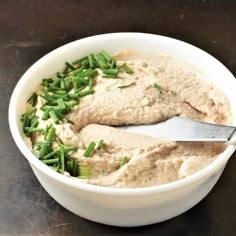 a white bowl filled with hummus and green onions on top of a black table