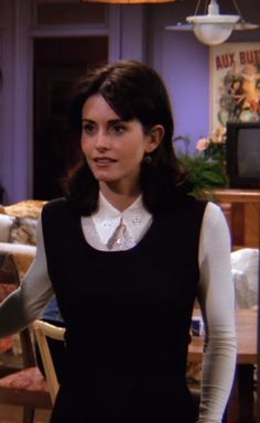 the young woman is wearing a black dress and white collared shirt, with her hands in her pockets