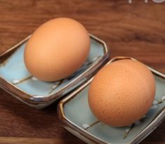 two brown eggs sitting in small dishes on a wooden table