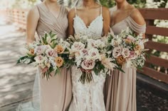 three bridesmaids holding their bouquets in front of a wooden fence and trees