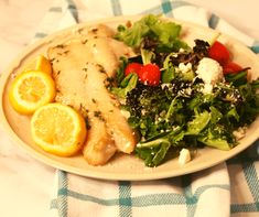 a white plate topped with chicken, salad and lemon slices