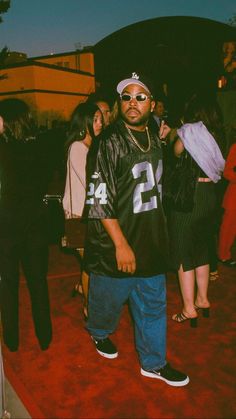 a man standing on top of a red carpet next to other people and wearing sunglasses