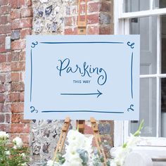 a blue sign that says parking this way next to some flowers in front of a brick building