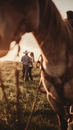 two people are walking through the grass with a horse in the background