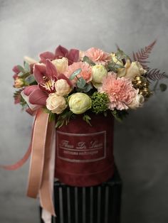 a red bucket with flowers and greenery in it on a black stand against a gray background