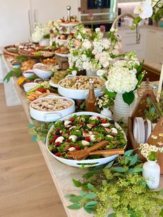 a table filled with lots of food and flowers on top of it, including salads