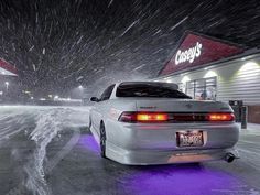 a white car parked in front of a store on a snowy day with snow falling