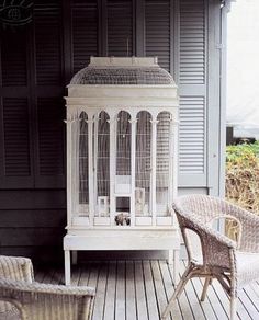 a white birdcage sitting on top of a wooden floor next to two wicker chairs