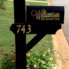 a black mailbox sitting on the side of a road with flowers growing in it