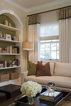 a living room filled with furniture and bookshelves next to a window covered in curtains