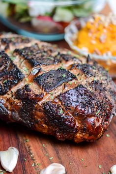 a piece of meat sitting on top of a wooden cutting board next to garlic and other foods