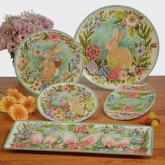 an assortment of easter themed plates and bowls on a wooden table with flowers in the background