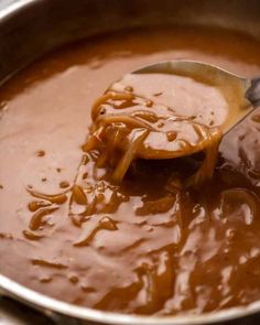 a ladle full of caramel sauce being stirred with a spoon