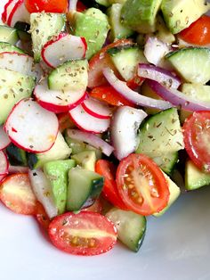 a white plate topped with cucumber, tomatoes and radishes on top of it