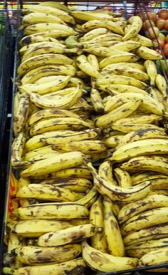 several bunches of bananas are on display in a grocery store with other fruits and vegetables behind them