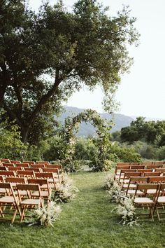 an outdoor ceremony setup with wooden chairs and greenery