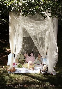 a canopy bed with teddy bears and other toys on it in the grass under a tree