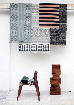 a chair sitting in front of a wall hanging with different colored rugs