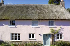 a pink house with a thatched roof and white trim on the front door is surrounded by greenery