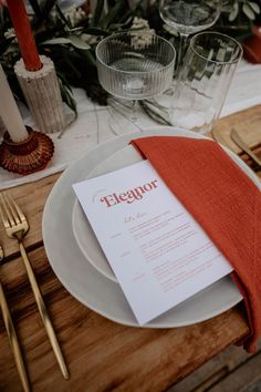 a place setting with an orange napkin, silverware and red napkin on the plate