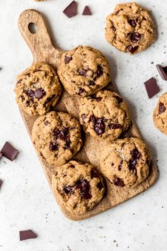 chocolate chip cookies on a cutting board next to pieces of chocolate chips and a wooden spoon