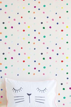 a cat pillow sitting on top of a bed next to a wall with colorful dots