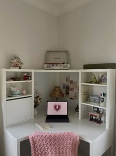 a laptop computer sitting on top of a white desk next to a shelf filled with books