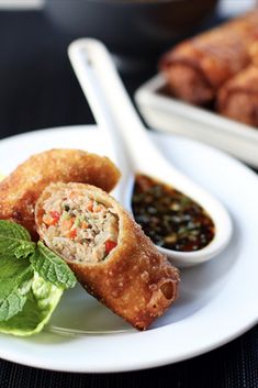 some food is on a white plate with green leaves and dipping sauce in the bowl