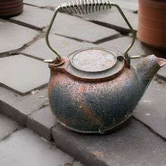 an old teapot sitting on the ground next to potted plants